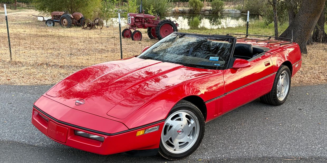 Red convertible Corvette parked near a farm fence.