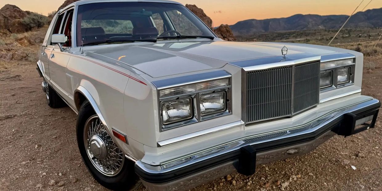 Classic white vintage car parked in a desert landscape during sunset.