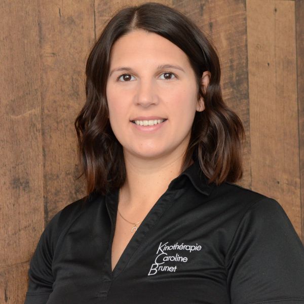 Woman in black shirt with a friendly smile, standing against a wooden backdrop.