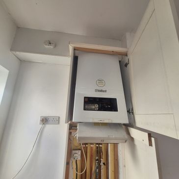 Wall-mounted Vaillant boiler installed inside a wooden cabinet in a utility room.