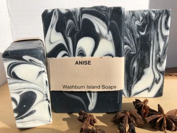 Soap bars with black charcoal and white colours. There is a brown paper wrap around one of the bars.