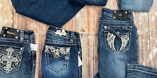 Five pairs of embellished blue jeans laid out on a wooden floor.