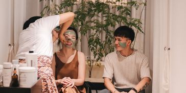Two people having green facial masks applied in a cozy setting.