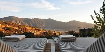 Sunset view over mountain hills from a cozy outdoor lounge area with striped cushions.