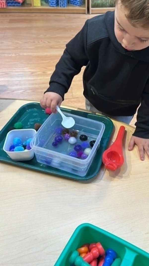 a child at a table scooping ice cubes out of water with a spoon