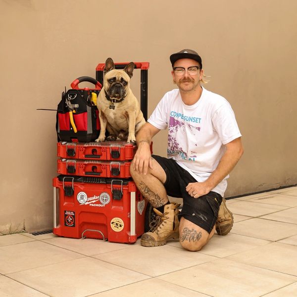 Electrician with a French bulldog sitting on toolboxes, ready for work with tools in hand.