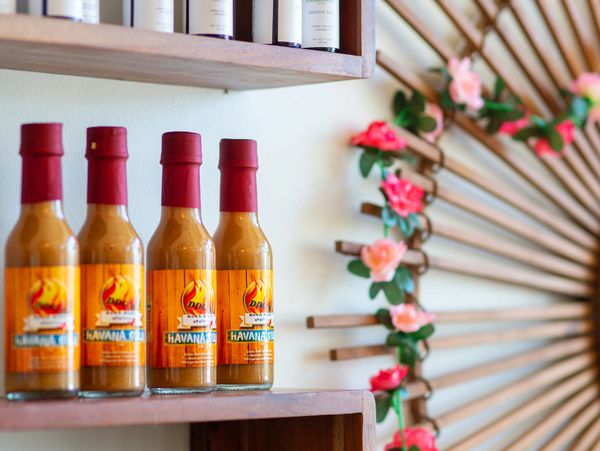 Four bottles of hot sauce lined up on a wooden shelf.