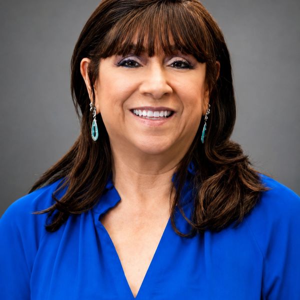 Smiling woman in blue blouse with earrings.
