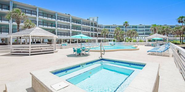 Sunny outdoor pool and hot tub area at a modern hotel with palm trees.