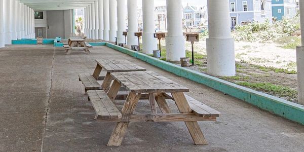 Empty wooden picnic tables under a covered pavilion with white columns.