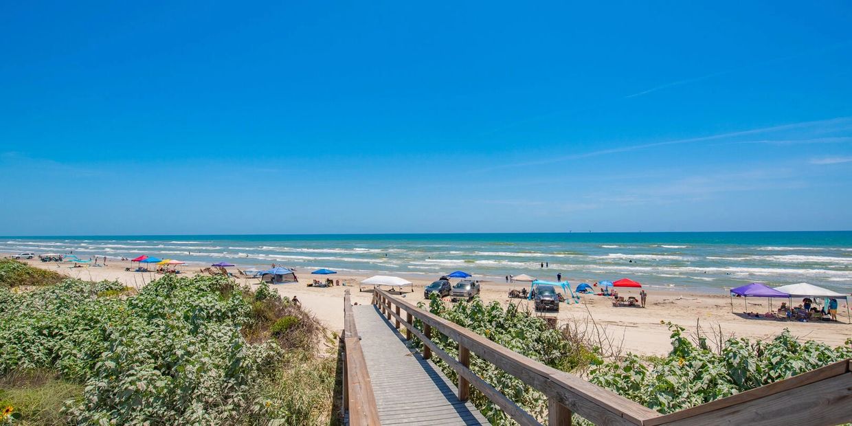 Wooden boardwalk leading to a beach with colorful tents and vehicles.