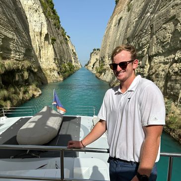 Man smiling on a boat in a narrow canal between tall cliffs.