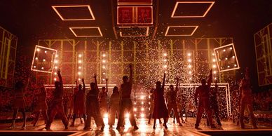 Silhouetted dancers performing on stage with bright lights and confetti.