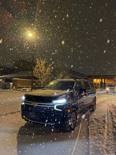 Black SUV in snowy night with headlights on.