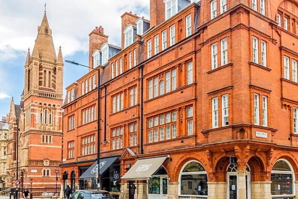 Historic red brick buildings and a church tower in a lively city street. Flats for sale London Property real estate listings 