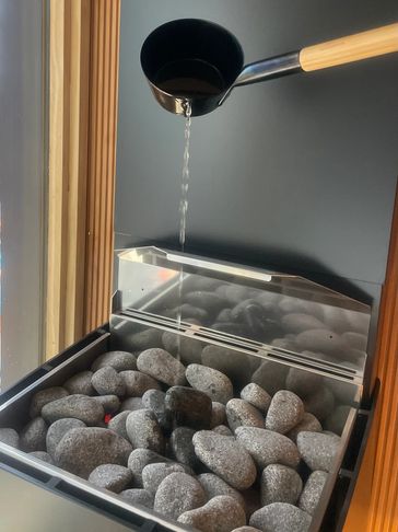 Water being poured onto hot sauna stones from a wooden-handled ladle.