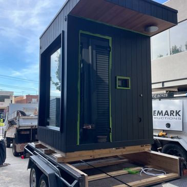 A small modern black structure on a trailer, possibly a tiny house or booth.