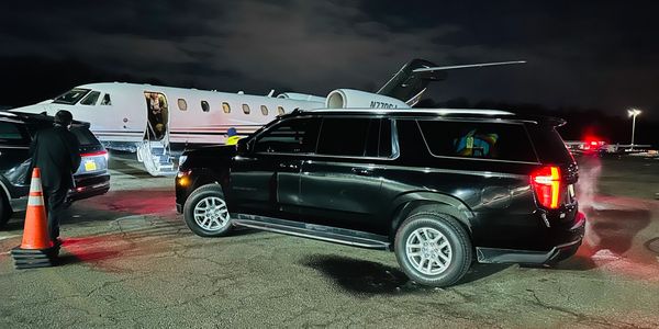 A black SUV parked near a private jet at night with people around.