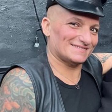 Person smiling, wearing a leather vest and cap.