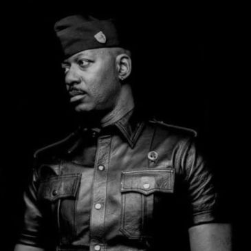 Man in leather jacket and cap looking to the side.