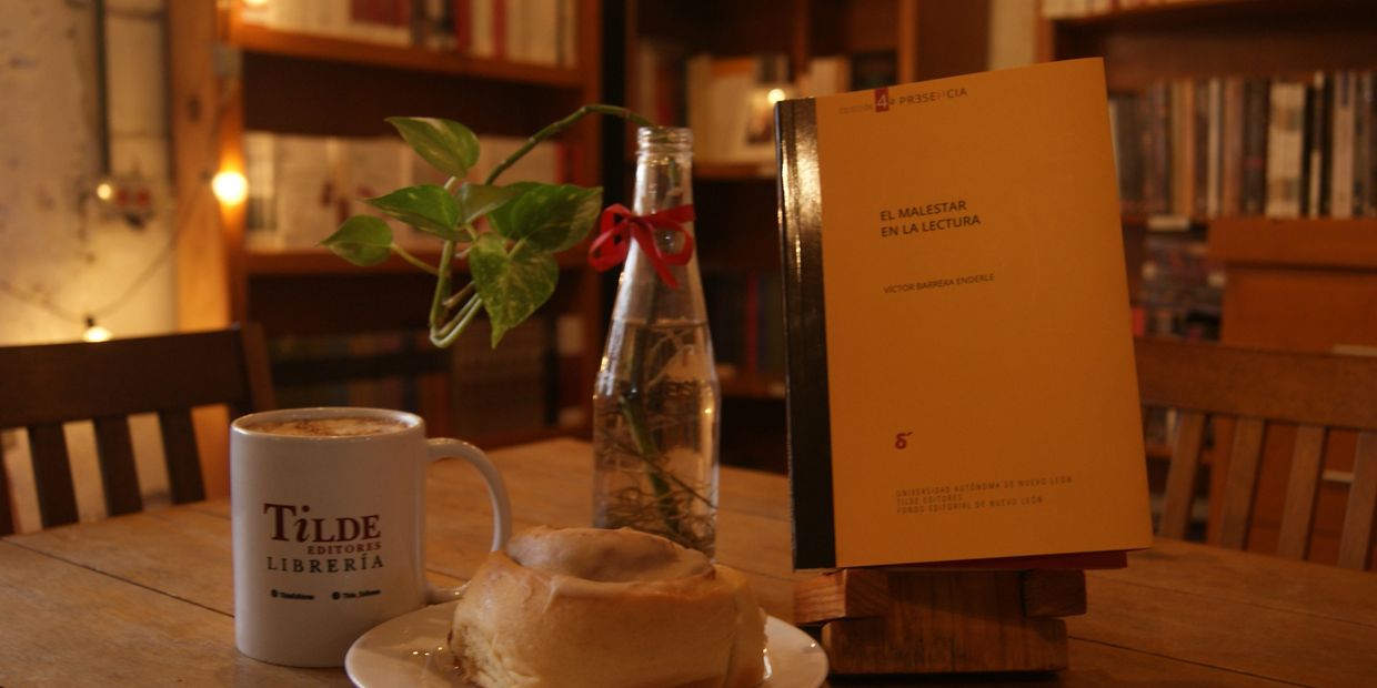 Cozy reading setup with coffee, pastry, and a book in a warm library setting.