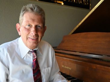 A gentleman sitting in front of a brown Kawai baby grand piano