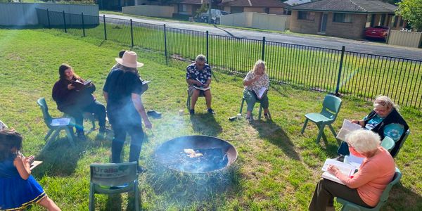 Group of people sitting in a circle around a small fire pit outdoors.