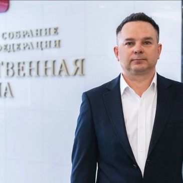Man in suit standing in front of a wall with Russian text.