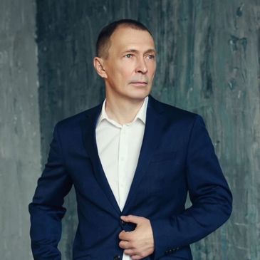 Man in a navy blue suit adjusting his jacket, looking contemplative.
