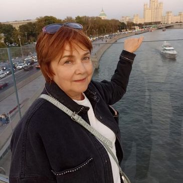 Woman posing on a bridge with river and cityscape in the background.