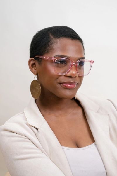 Confident woman wearing pink glasses and large earrings smiles subtly.