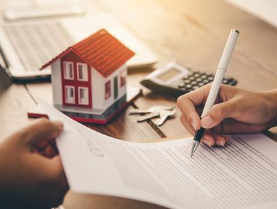 Signing a contract with a toy house, calculator, and keys in the background