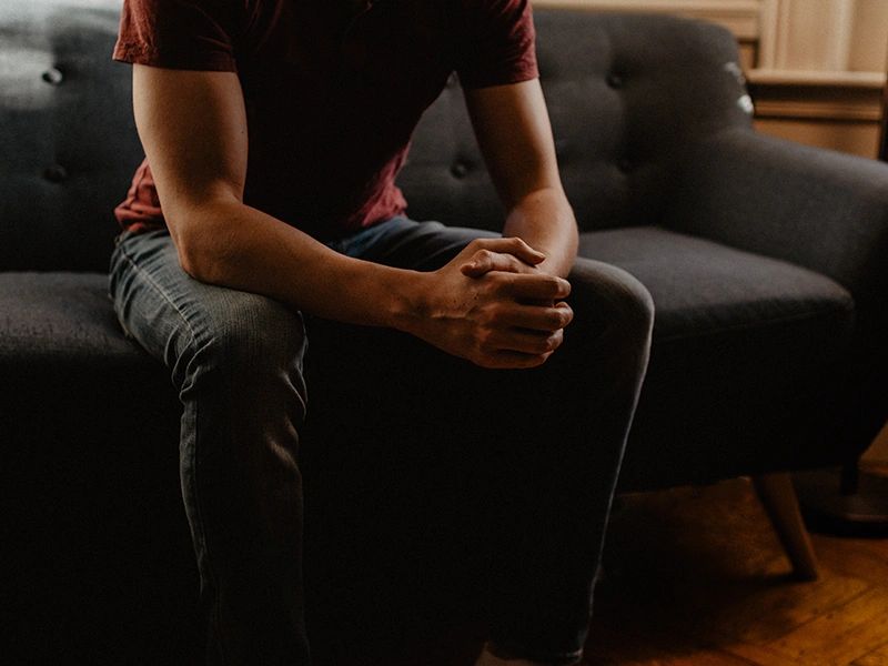man from shoulders down sitting on couch with hands clasped