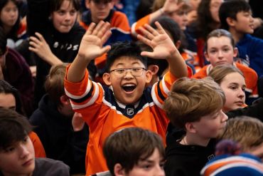 Excited boy in an orange sports jersey waving enthusiastically.