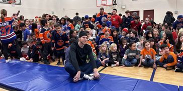Crowd of children and adults gathered in a gym, some wearing sports jerseys.