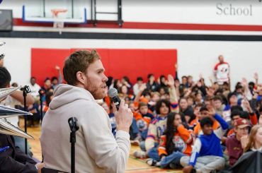 Man speaking to a group in a school gym.