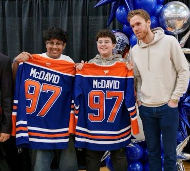 Two boys holding McDavid jerseys, standing with a man.