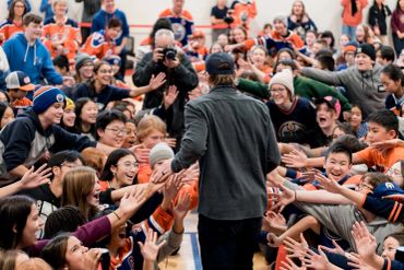 Man greeting excited crowd in gymnasium.