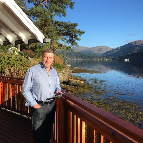 Man standing on a balcony overlooking a lake and mountains.