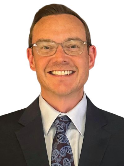 Smiling man in a suit with glasses and paisley tie.
