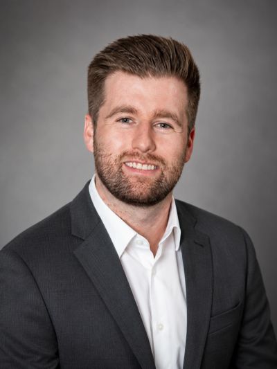 Professional man in a dark suit smiling against a gray background.