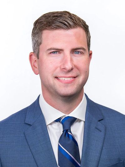 Professional headshot of a man in a blue suit and striped tie.