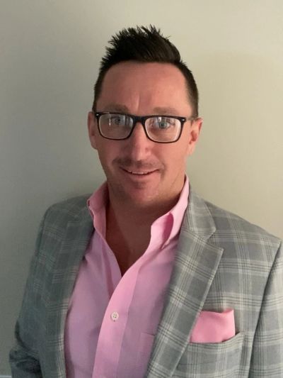 Man wearing glasses, a pink shirt, and a gray checkered blazer.