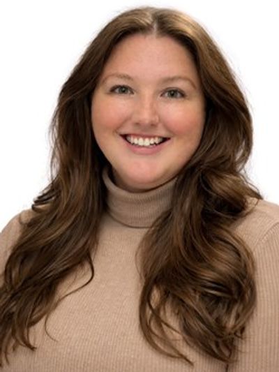 Smiling woman with long brown hair wearing a beige turtleneck sweater.