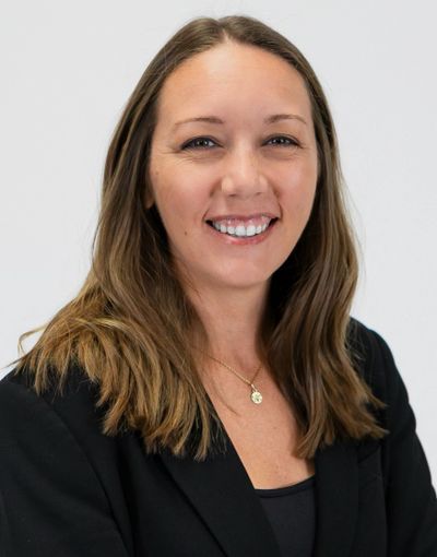 Smiling woman with long hair in a black blazer against a white background.
