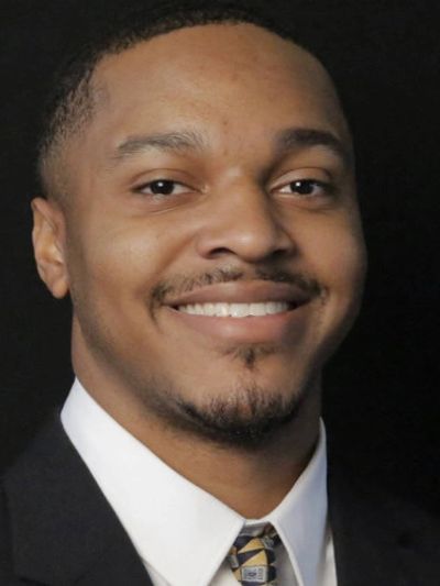 Smiling man in formal suit and tie against a black background.