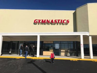 A child stands in front of a gymnastics center on a sunny day.
