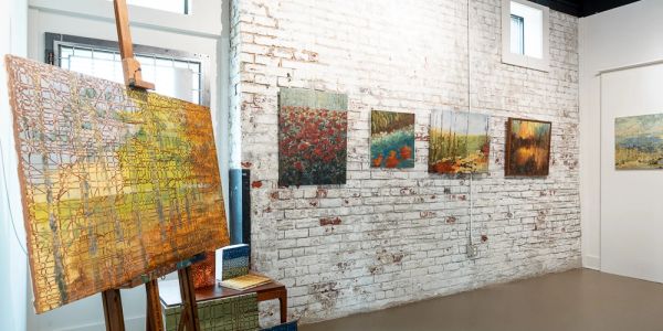 Art gallery with paintings on white brick wall and an easel.