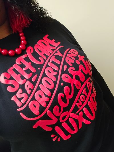 Person wearing a black shirt with bold red self-care message.