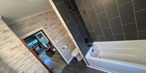 Modern bathroom with black tiles and a white bathtub.